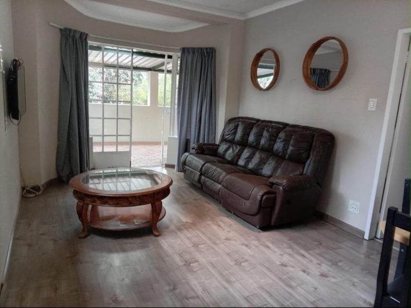 A comfortable living room featuring laminate flooring, coved ceilings, and a sliding glass door providing access to an outdoor patio area.