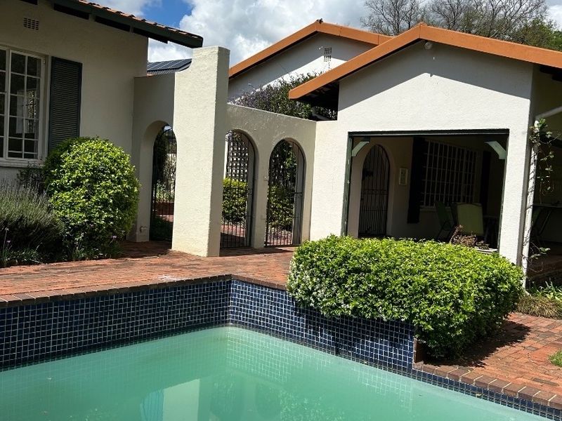 Outdoor pool area featuring a tiled swimming pool, brick paving, and architectural arched masonry walls connecting the building structures.
