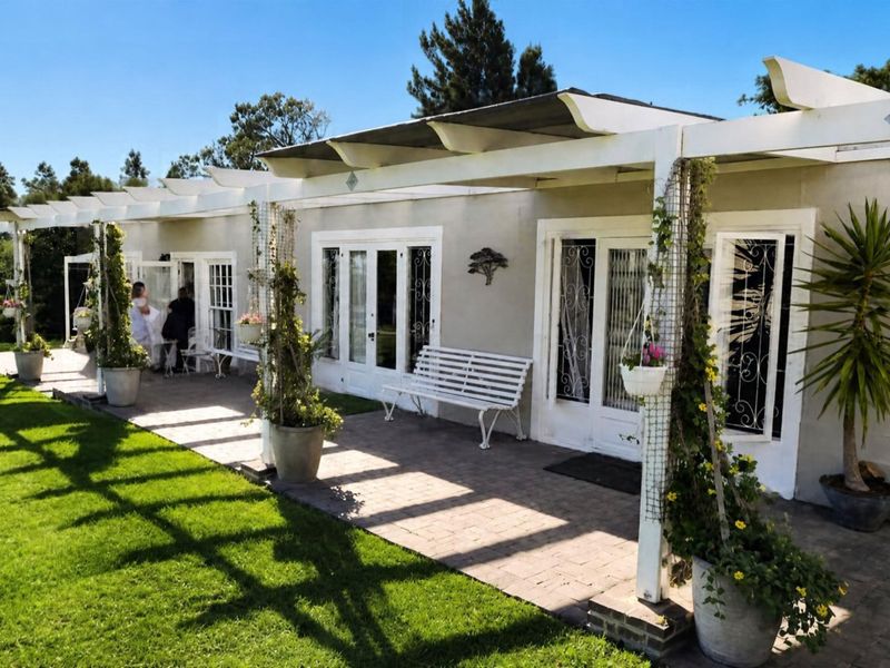A spacious paved patio area featuring a white pergola structure, providing direct access to the home through multiple sets of french doors.