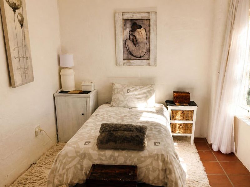 A cozy bedroom featuring terracotta floor tiles and a multi-pane window with security bars, offering a bright and inviting atmosphere.