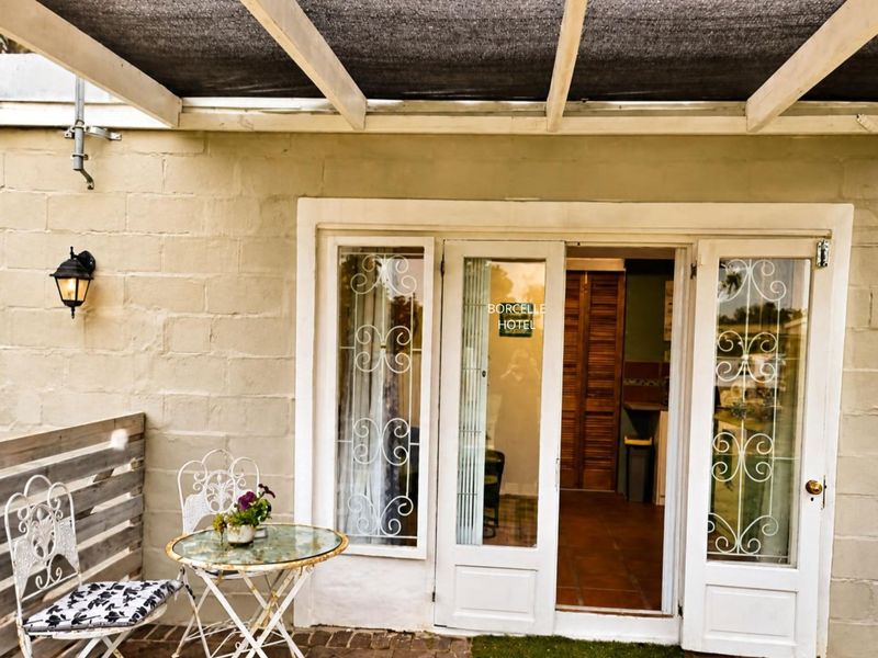 A covered patio area featuring a pergola with shade cloth, cinder block walls, and white french doors providing access to the interior.