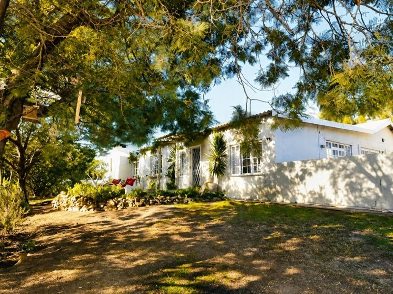 Rear view of the farm property featuring a white facade, tiled roof, and established garden with a stone retaining wall.