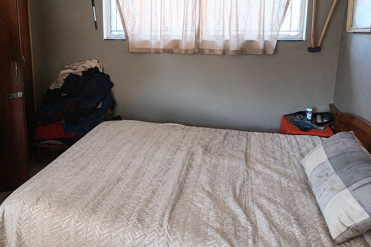 A bedroom featuring a built-in wardrobe and security bars on the window, requiring cosmetic updates to the wall finishes.