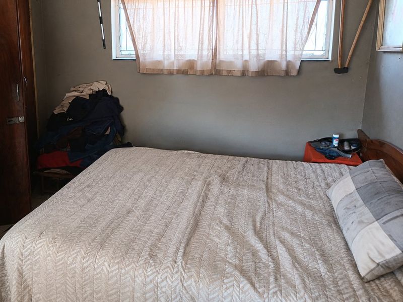 A bedroom featuring a built-in wardrobe and security bars on the window, requiring cosmetic updates to the wall finishes.