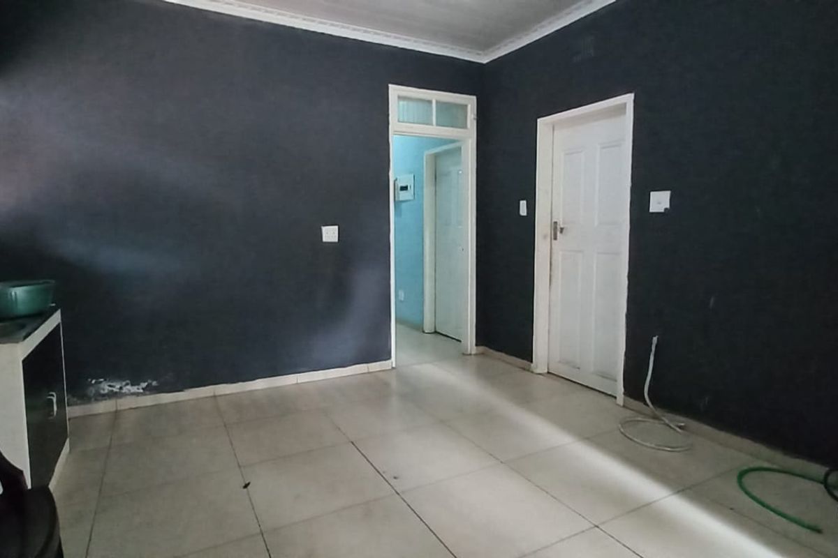 A basic, empty kitchen area featuring tiled flooring, dark painted walls, and a built-in sink unit, requiring cosmetic updates to improve its appeal.