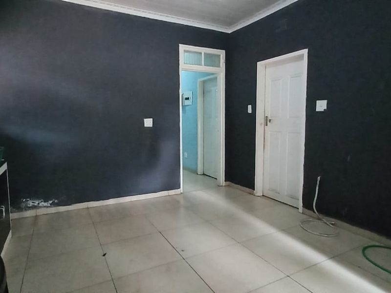 A basic, empty kitchen area featuring tiled flooring, dark painted walls, and a built-in sink unit, requiring cosmetic updates to improve its appeal.