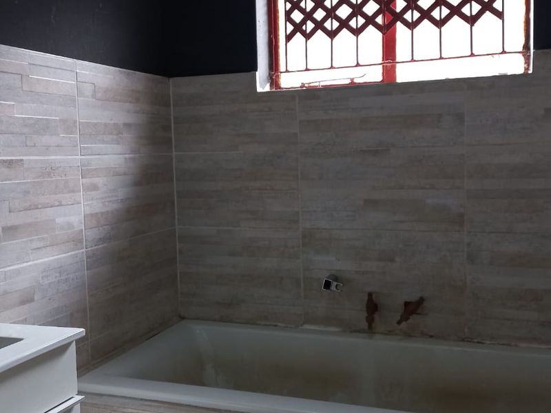 A bathroom featuring tiled walls and a built-in bathtub, currently requiring plumbing fixture installation and cosmetic updates to the tub area.