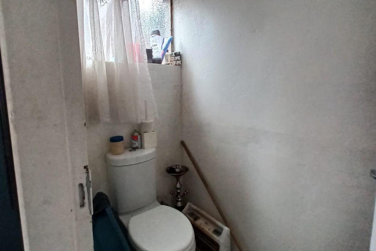 A small, dated bathroom featuring a standard toilet and an obscured glass window, requiring cosmetic updates and wall refinishing.
