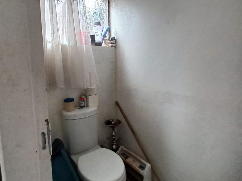 A small, dated bathroom featuring a standard toilet and an obscured glass window, requiring cosmetic updates and wall refinishing.