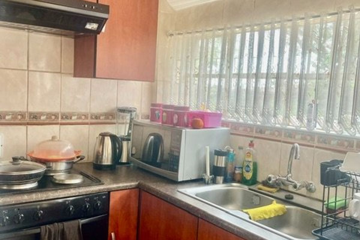 A functional kitchen featuring laminate cabinetry, a double bowl stainless steel sink, built-in oven, hob, and extractor fan with tiled splashbacks.