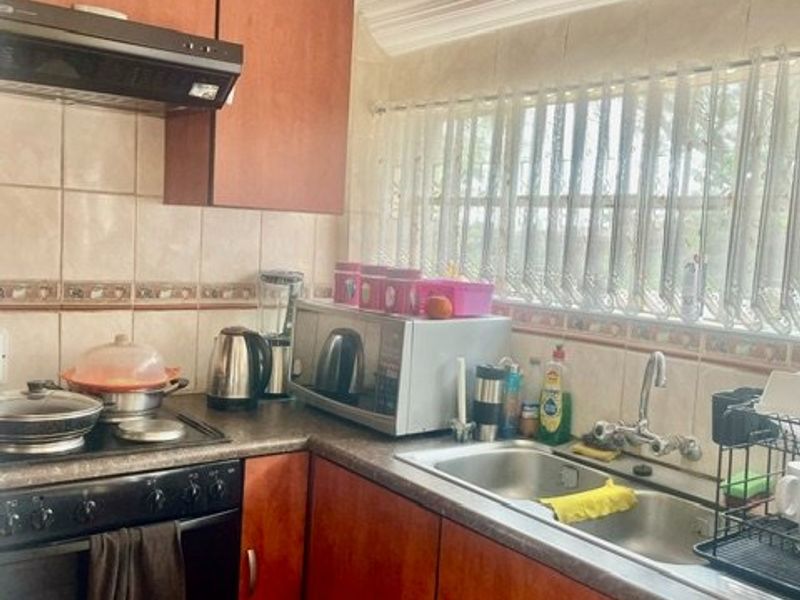 A functional kitchen featuring laminate cabinetry, a double bowl stainless steel sink, built-in oven, hob, and extractor fan with tiled splashbacks.
