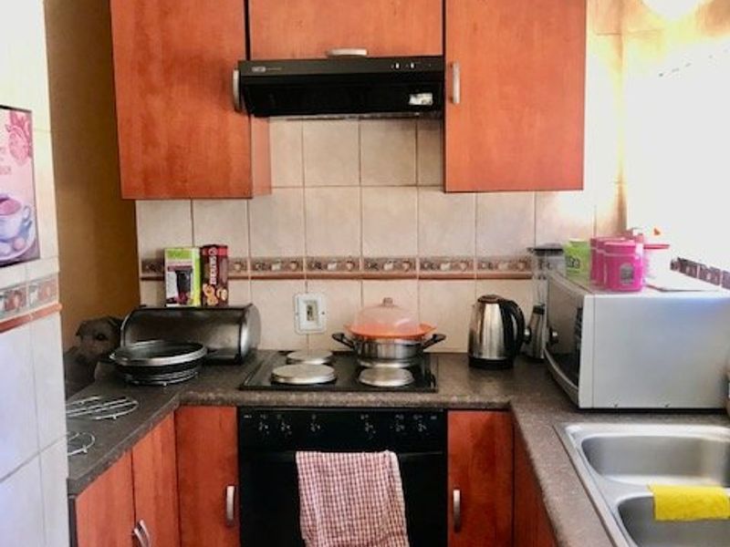 Compact kitchen featuring built-in cabinetry, electric hob, oven, extractor fan, and a double bowl sink with tiled backsplash and tongue and groove ceiling.