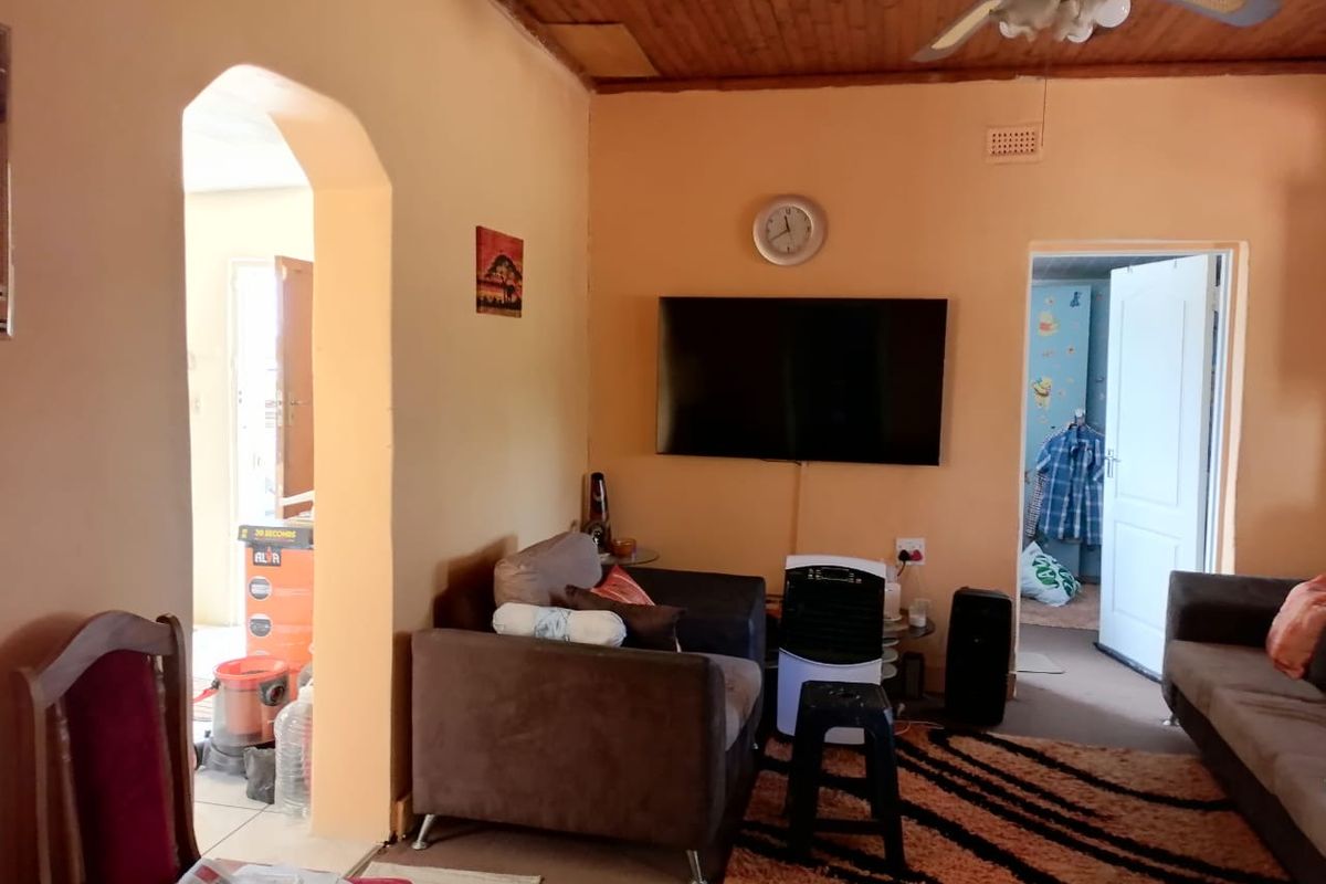 A living room featuring a timber ceiling with a fan, an arched doorway, and wall-mounted television, requiring cosmetic updates to improve the overall aesthetic.