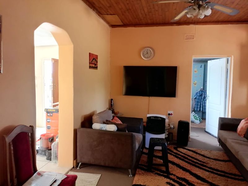A living room featuring a timber ceiling with a fan, an arched doorway, and wall-mounted television, requiring cosmetic updates to improve the overall aesthetic.