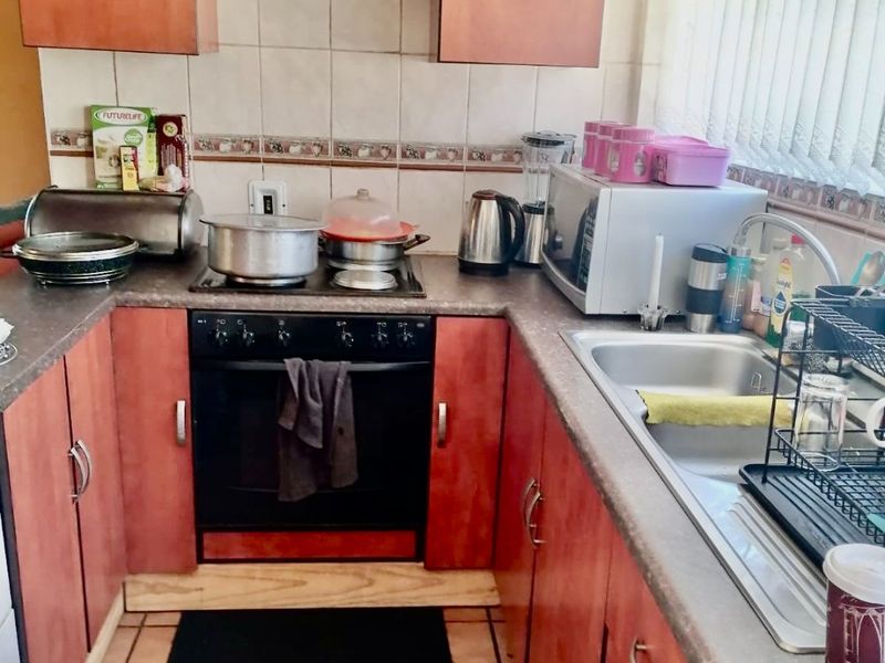 A compact kitchen featuring dated wood-look cabinetry, tiled backsplash, built-in oven with extractor fan, and a stainless steel sink.