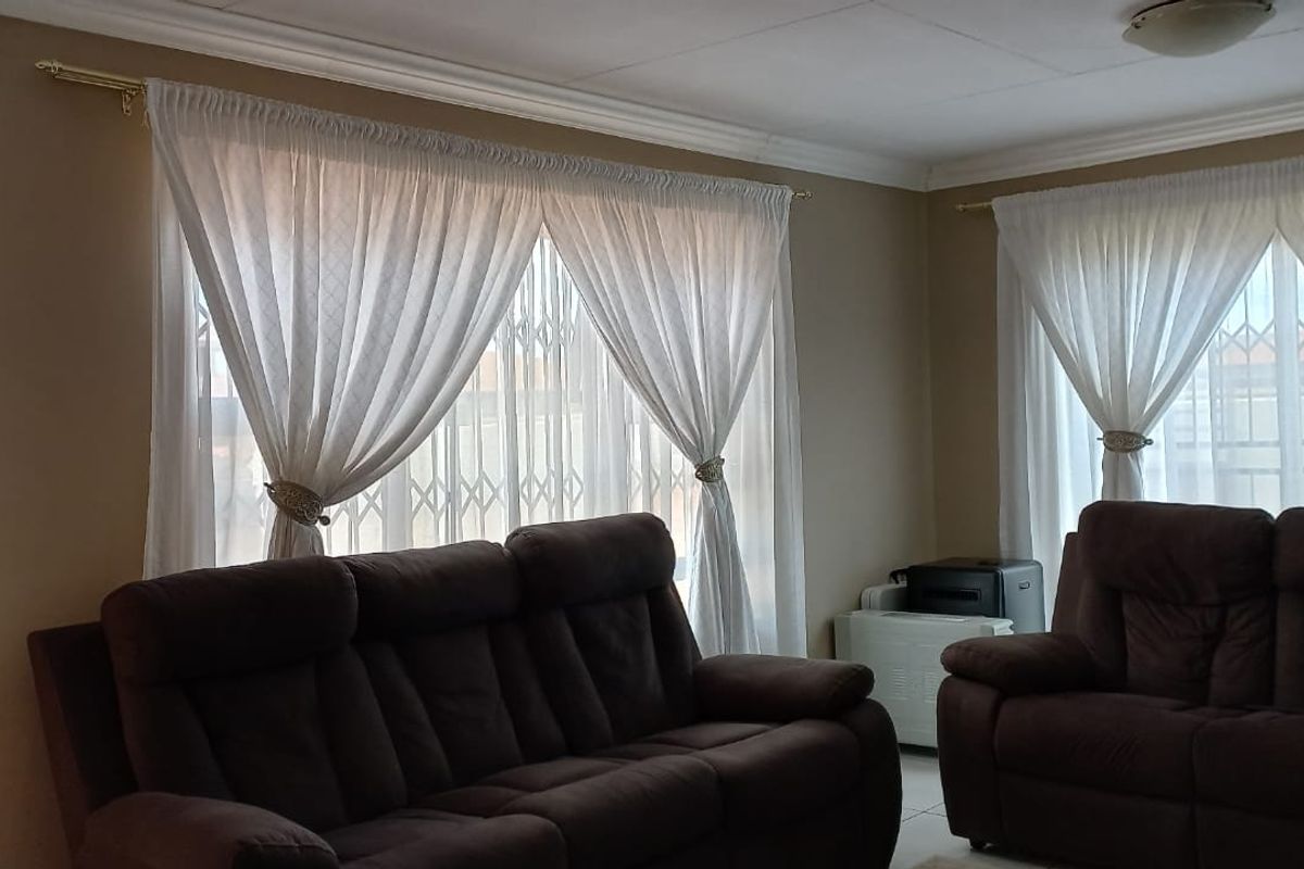 A comfortable living room featuring tiled flooring, coving, and a wall-mounted air conditioning unit, with security gates installed on the windows.