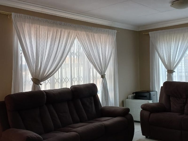 A comfortable living room featuring tiled flooring, coving, and a wall-mounted air conditioning unit, with security gates installed on the windows.