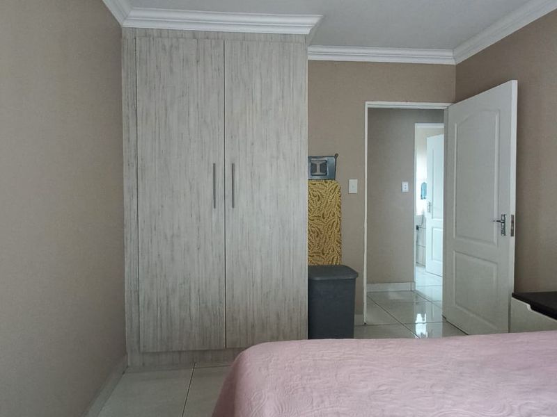 A well-maintained bedroom featuring built-in cupboards, crown molding, and neutral tiled flooring, with an open doorway leading to an adjacent space.