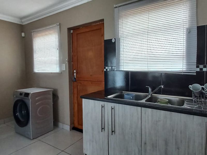 A functional laundry room featuring tiled flooring, built-in cabinetry with a double basin sink, and direct access to the exterior via a timber door.