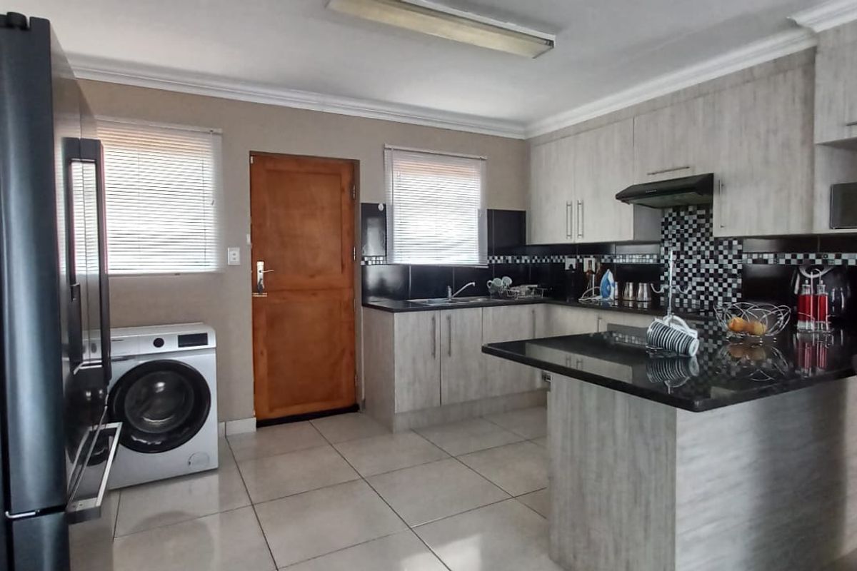 A functional kitchen featuring light wood-finish cabinetry, granite countertops, mosaic tile backsplash, and tiled flooring with integrated laundry space.