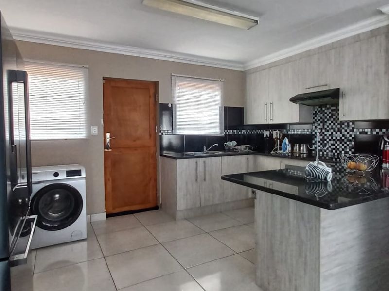 A functional kitchen featuring light wood-finish cabinetry, granite countertops, mosaic tile backsplash, and tiled flooring with integrated laundry space.