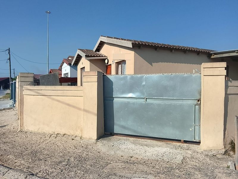 Front view of a residential property featuring a plastered facade, tiled roof, and a metal sliding gate set within a perimeter wall.