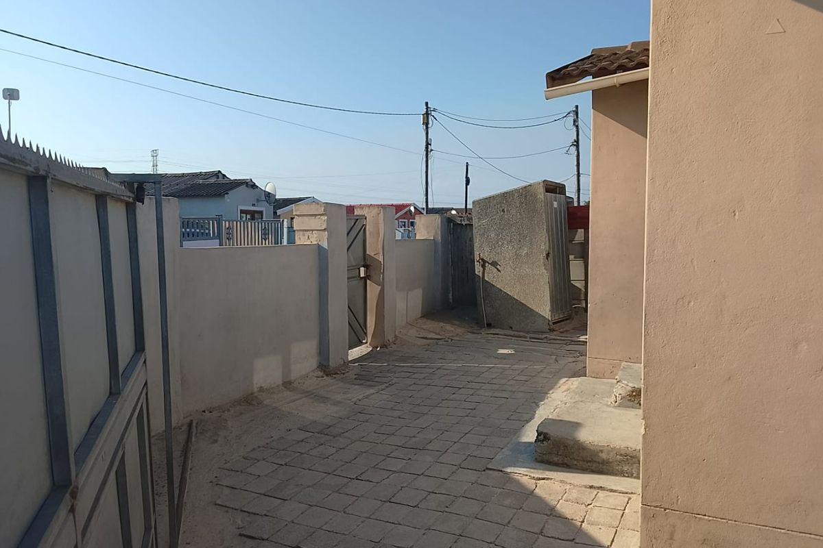 A side exterior area featuring paved walkways, boundary walls, and concrete steps leading to the property entrance.