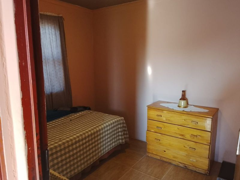 A compact bedroom featuring tiled flooring and a window, currently requiring cosmetic updates to improve its overall appeal and condition.