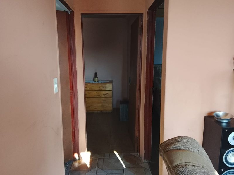 A narrow interior hallway connecting multiple rooms, featuring tiled flooring and painted walls in need of maintenance.