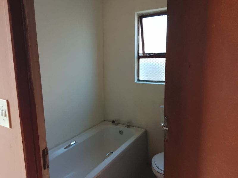 A compact, empty bathroom featuring a standard bathtub, toilet, and a top-hung window, requiring cosmetic updates to improve its overall condition.