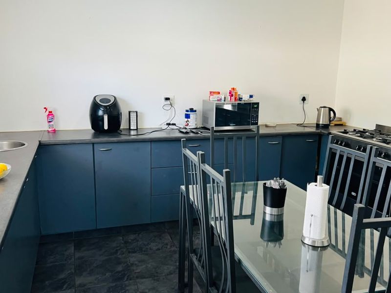 A functional kitchen featuring dark blue cabinetry, dark laminate countertops, a stainless steel sink, and a built-in gas hob and oven.