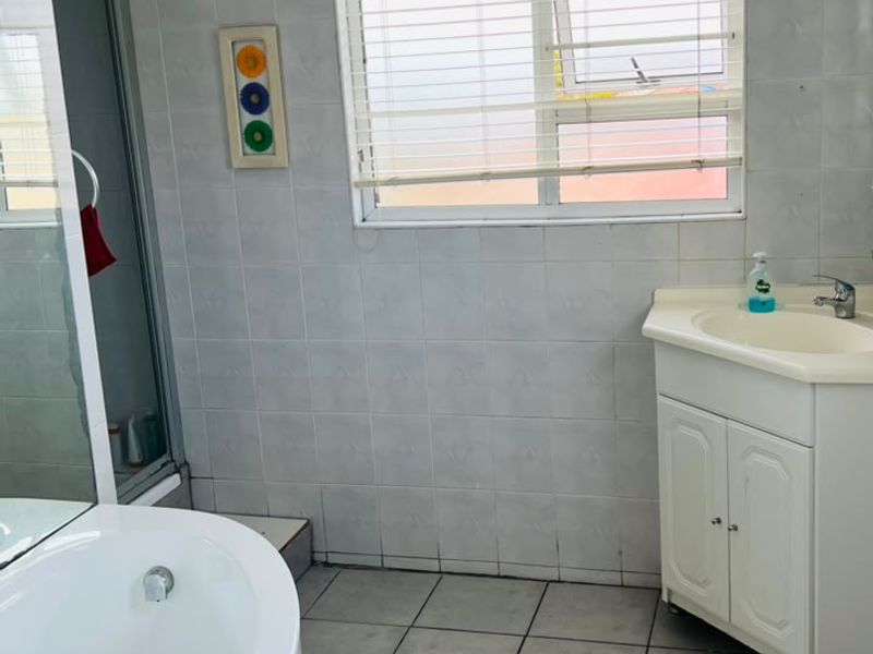 A functional bathroom featuring a corner bathtub, separate shower enclosure, vanity cabinet with basin, and tiled finishes throughout.
