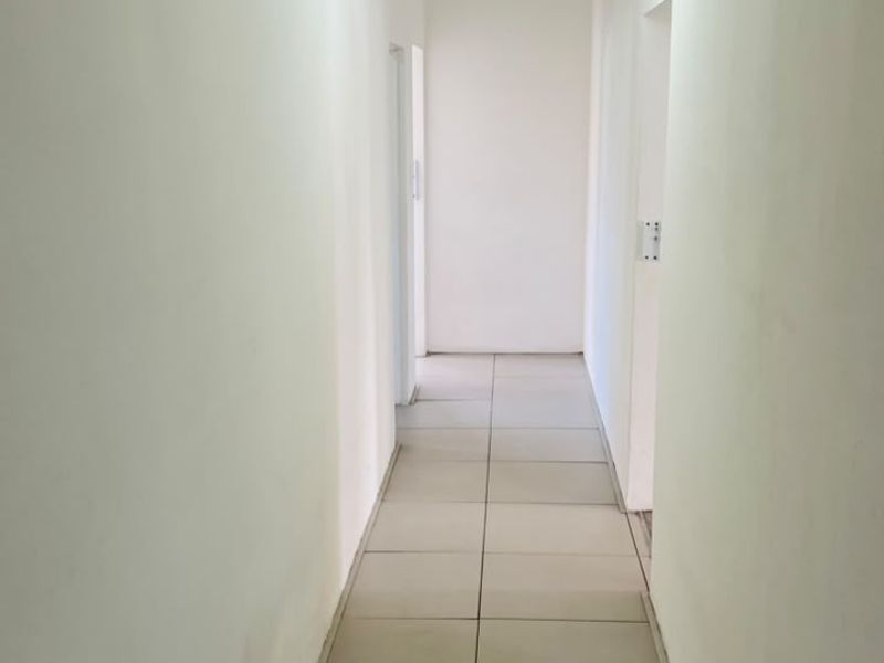 A clean, empty hallway featuring neutral tiled flooring and a modern pendant light fixture, providing a bright and functional transition space.