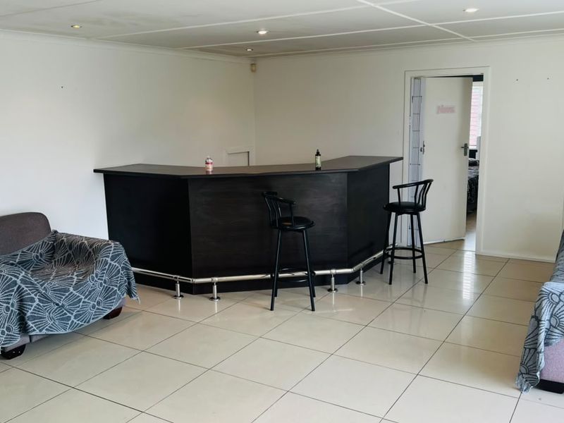 A dedicated bar area featuring a built-in dark wood counter with a foot rail, tiled flooring, and recessed ceiling lighting.