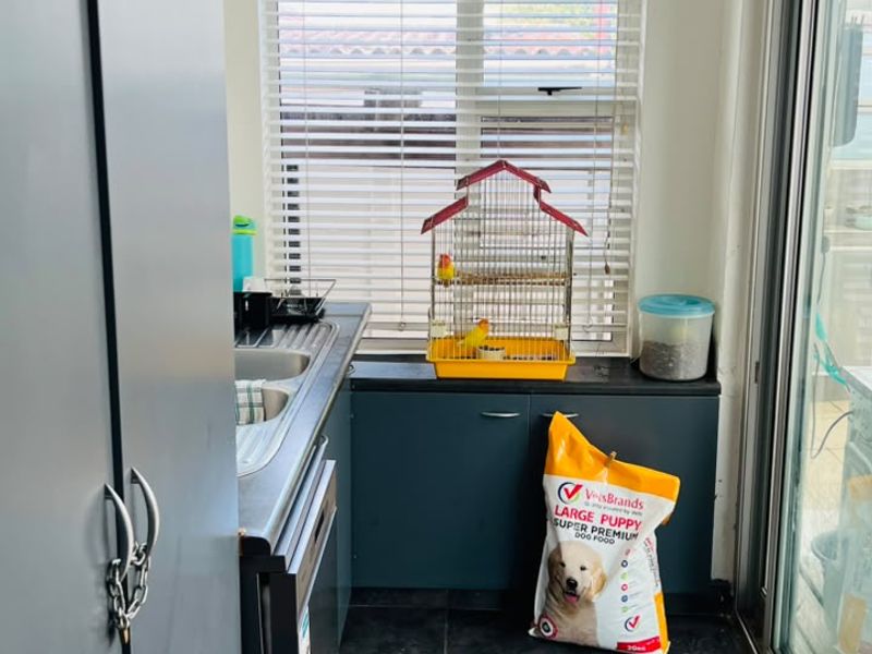 A functional laundry area featuring dark cabinetry, a stainless steel sink, tiled flooring, and direct access to the outdoors via a sliding glass door.