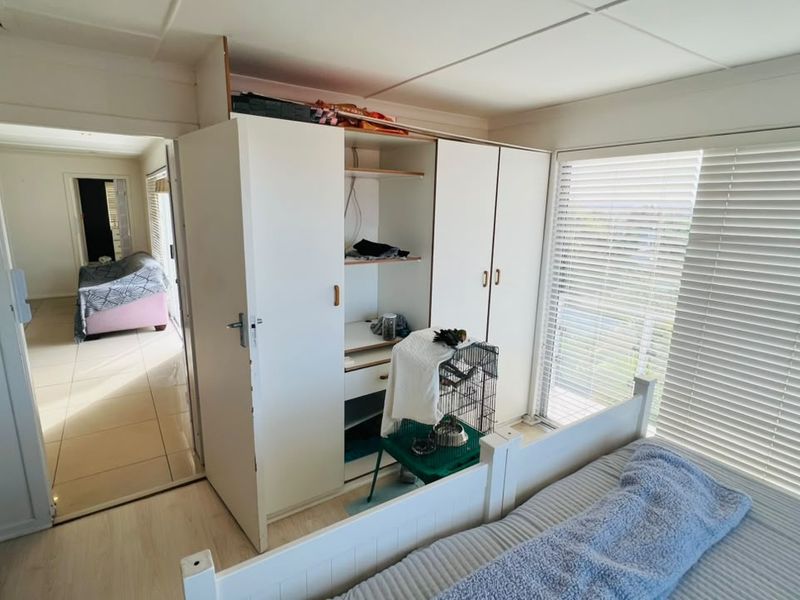 Bedroom featuring built-in wardrobe storage, light-toned flooring, and venetian blinds, offering a functional space with potential for cosmetic updates.