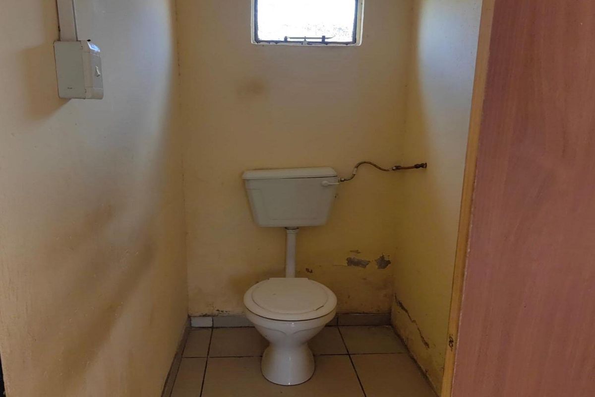 A small, dated bathroom featuring a standard toilet, tiled flooring, and a small window, currently requiring cosmetic updates and wall repairs.