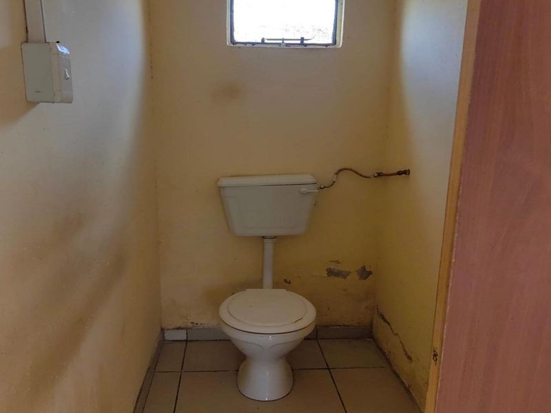 A small, dated bathroom featuring a standard toilet, tiled flooring, and a small window, currently requiring cosmetic updates and wall repairs.