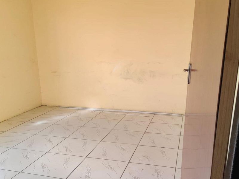 An empty bedroom featuring tiled flooring and a window with security bars, requiring minor cosmetic updates to the wall finishes.
