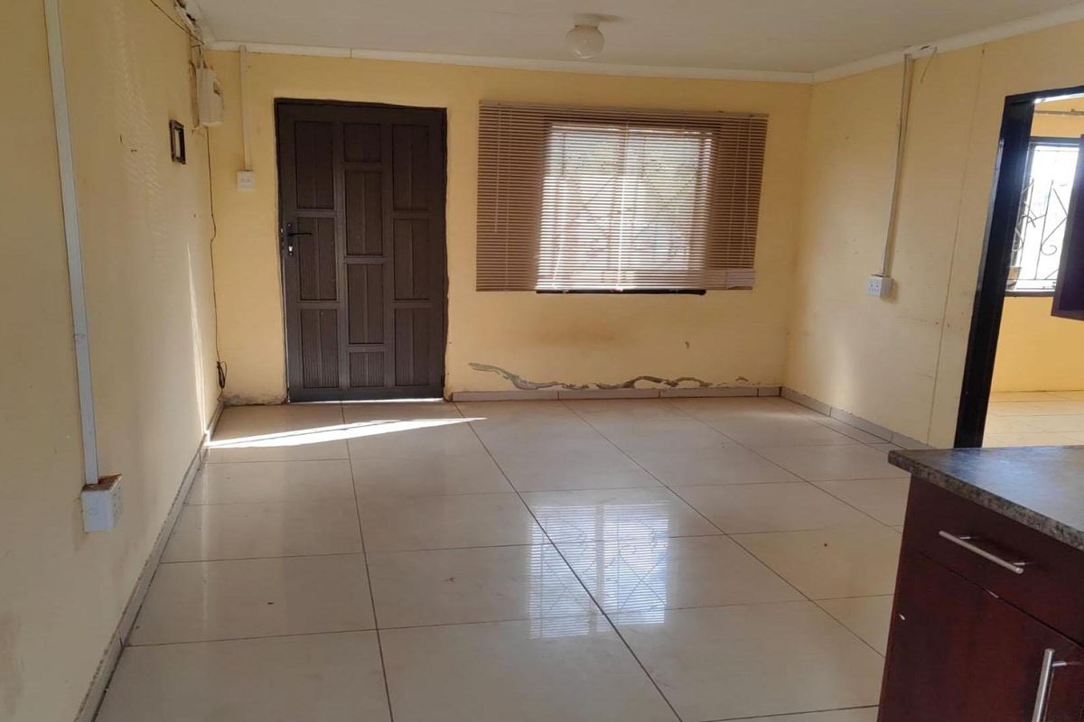 An empty open-plan living and kitchen area featuring tiled floors, built-in cabinetry, and natural light, requiring cosmetic updates to the walls.