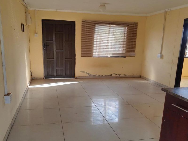 An empty open-plan living and kitchen area featuring tiled floors, built-in cabinetry, and natural light, requiring cosmetic updates to the walls.