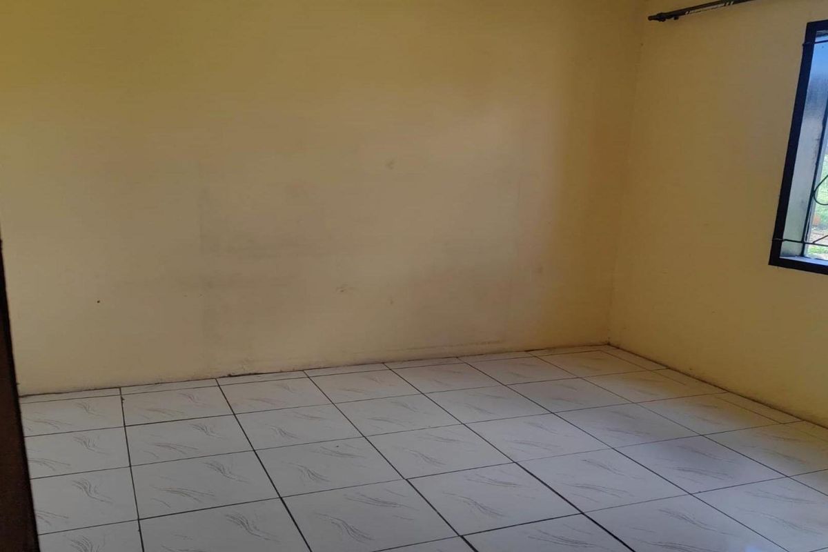 An empty bedroom featuring tiled flooring and a window fitted with a security gate, awaiting personal touches and updates.