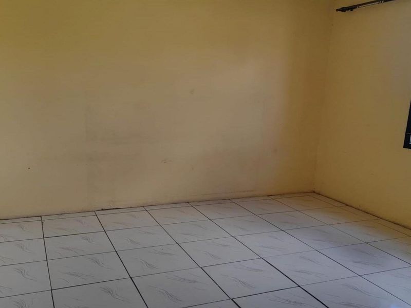 An empty bedroom featuring tiled flooring and a window fitted with a security gate, awaiting personal touches and updates.