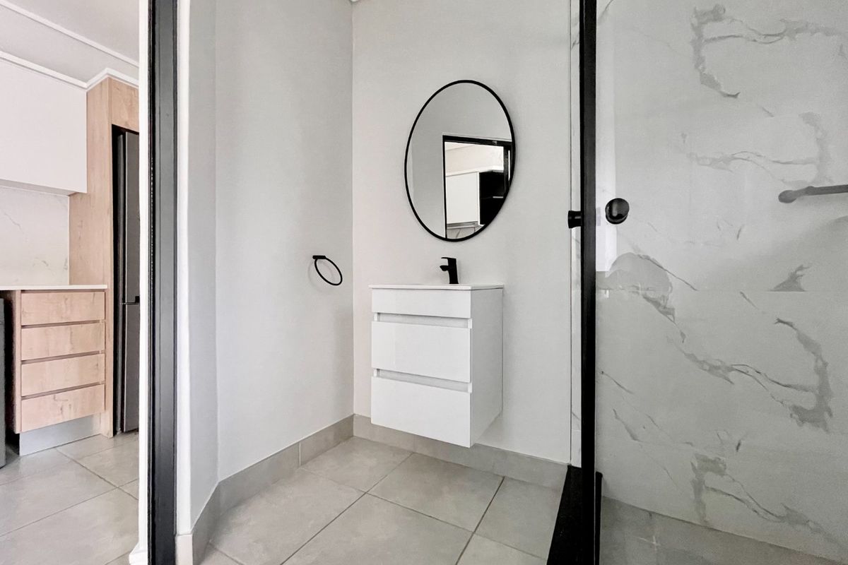 Modern bathroom featuring a wall-mounted vanity, black fixtures, and a walk-in shower with marble-look tiling.