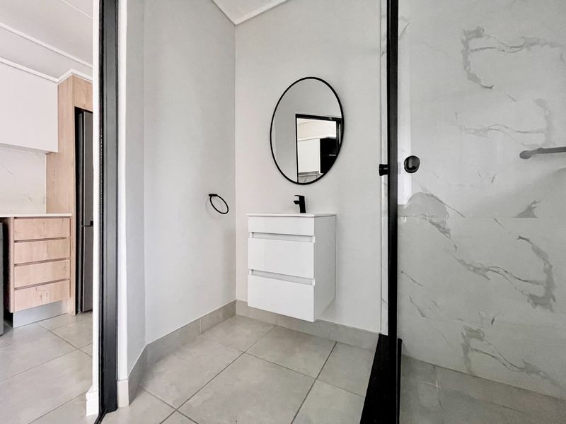 Modern bathroom featuring a wall-mounted vanity, black fixtures, and a walk-in shower with marble-look tiling.