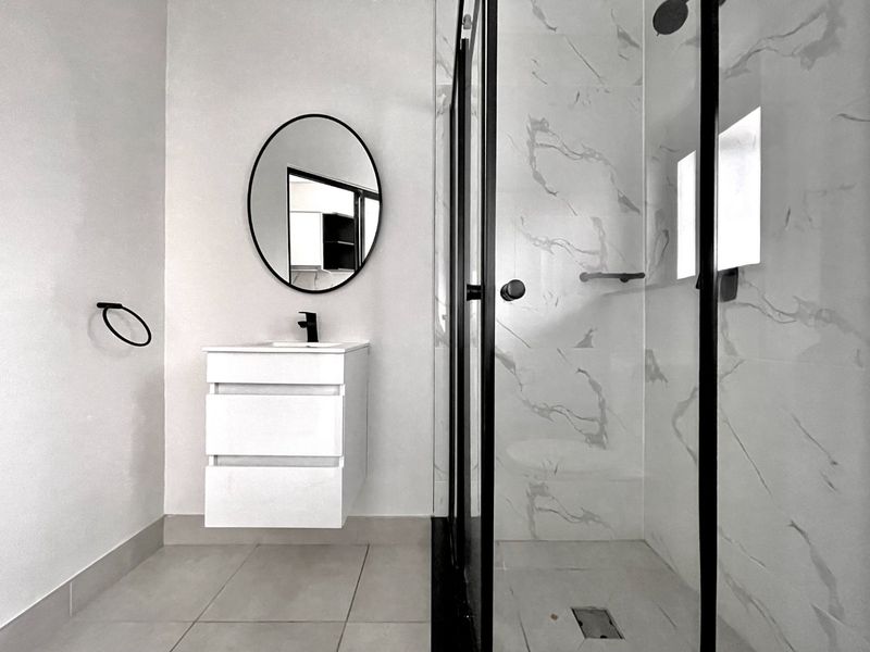 Modern bathroom featuring a wall-mounted vanity with integrated basin, black fixtures, and a walk-in shower with marble-look wall tiling.