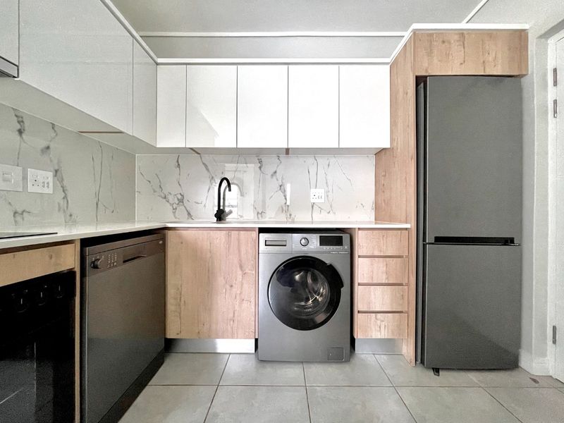Modern kitchen featuring sleek white and wood-grain cabinetry, marble-look splashback, stone countertops, and integrated appliance spaces with high-quality finishes.