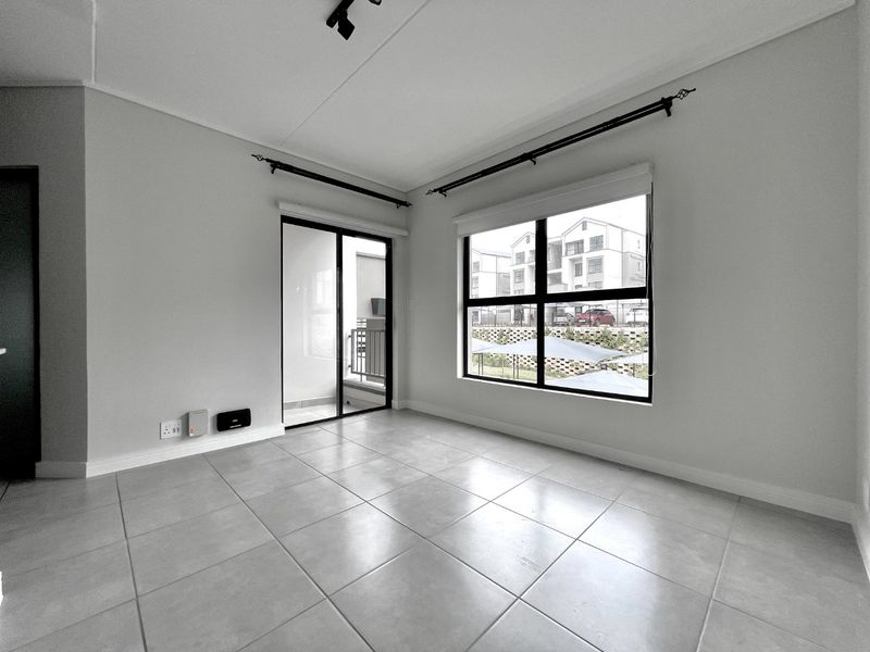 A bright, empty living area featuring neutral tiled flooring, large windows for natural light, and a sliding door leading to an outdoor space.