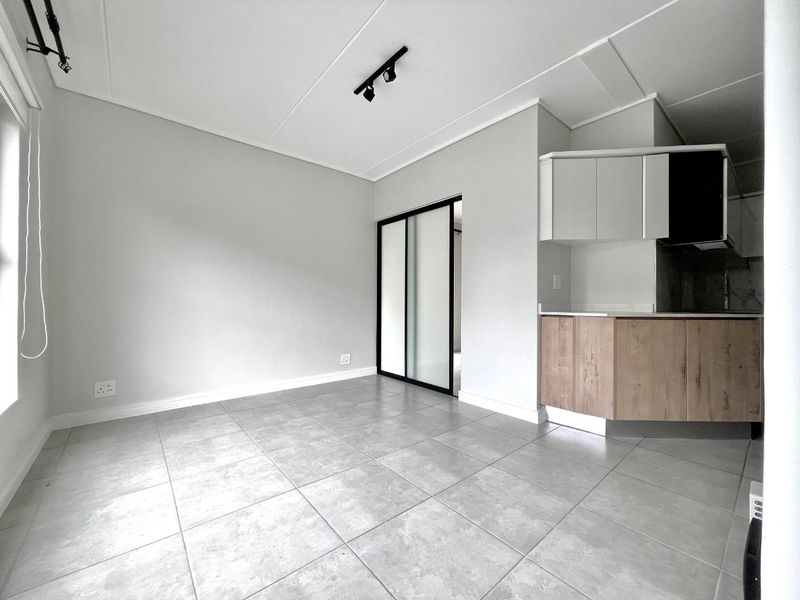 An open-plan living area featuring modern tiled flooring, neutral walls, and a compact kitchen with built-in cabinetry and stone countertops.