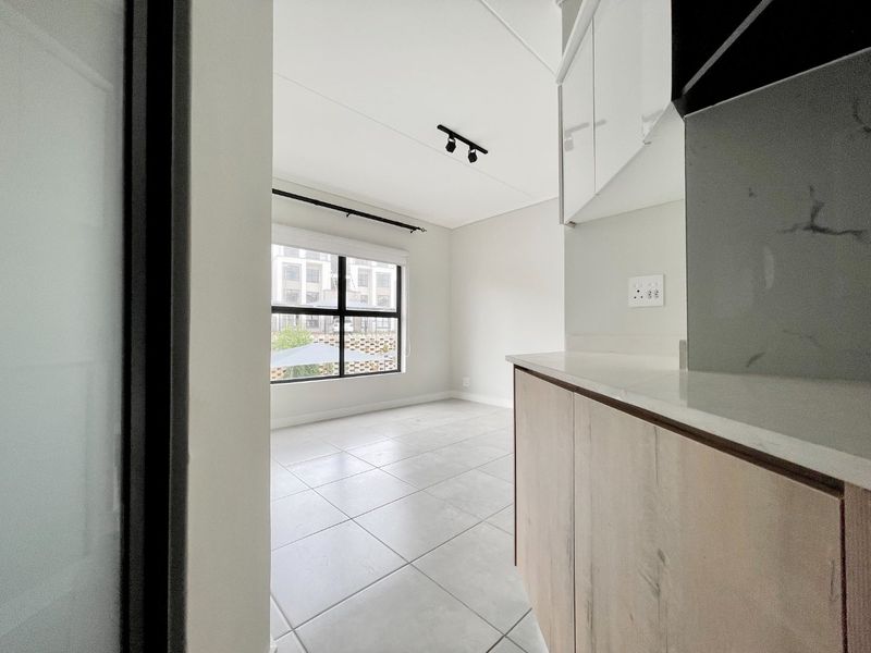 A bright, modern open-plan living and kitchen area featuring neutral tiled floors, contemporary track lighting, and sleek built-in cabinetry with stone countertops.
